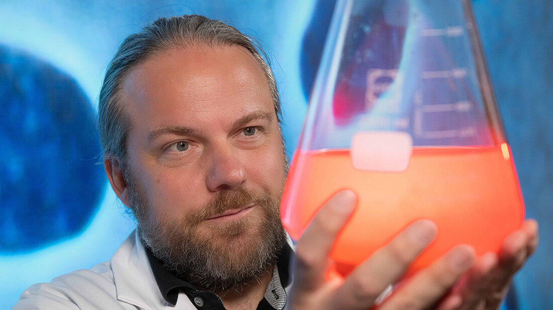 Mikrobiologe Prof. Dr. Christian Jogler blickt in ein Reagenzglas mit orangener Flüssigkeit