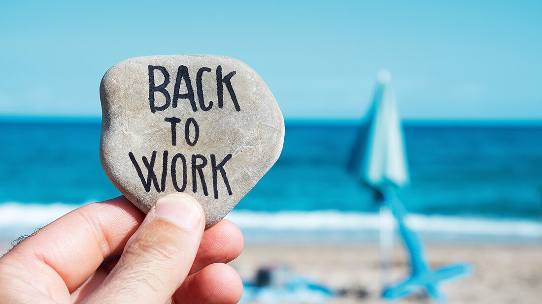 Foto von einem Strand, im Vordergrund ein Kiesel mit der Aufschrift: „Back to Work“