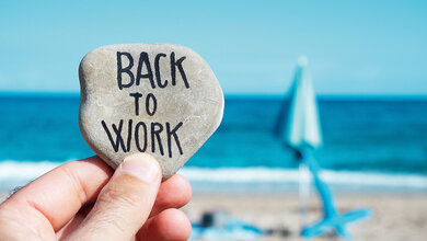 Foto von einem Strand, im Vordergrund ein Kiesel mit der Aufschrift: „Back to Work“