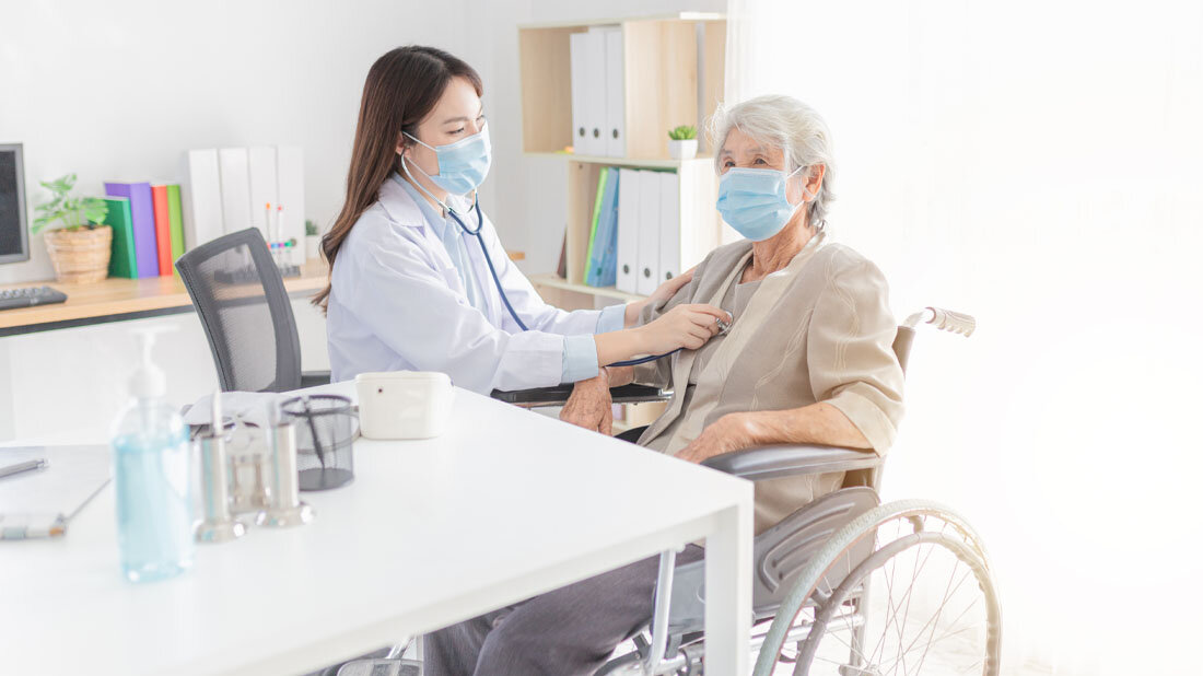 Ältere Frau im Rollstuhl wird von Ärztin abgehört