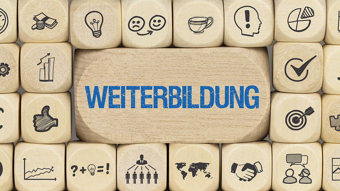 Foto von gestapelten Holzwürfeln mit verschiedenen Symbolen, in der Mitte ein hölzerner Quader mit der Aufschrift „WEITERBILDUNG“