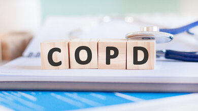 Holzwürfel mit den Buchstaben COPD auf einem unscharfen Notizblock, auf denen ein Stethoskop lehnt.