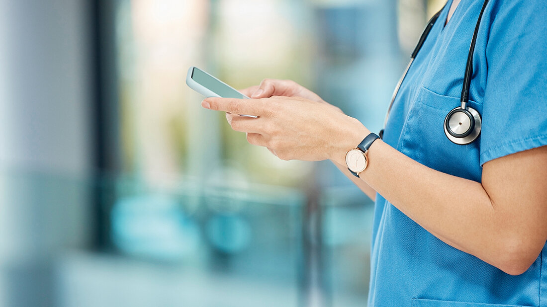 Mobiltelefone im Krankenhaus Foto einer Person in Medizinerkleidung bei der Bedienung eines Smartphones