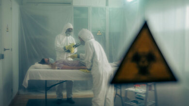 Personal mit Schutzanzügen untersucht eine Frau