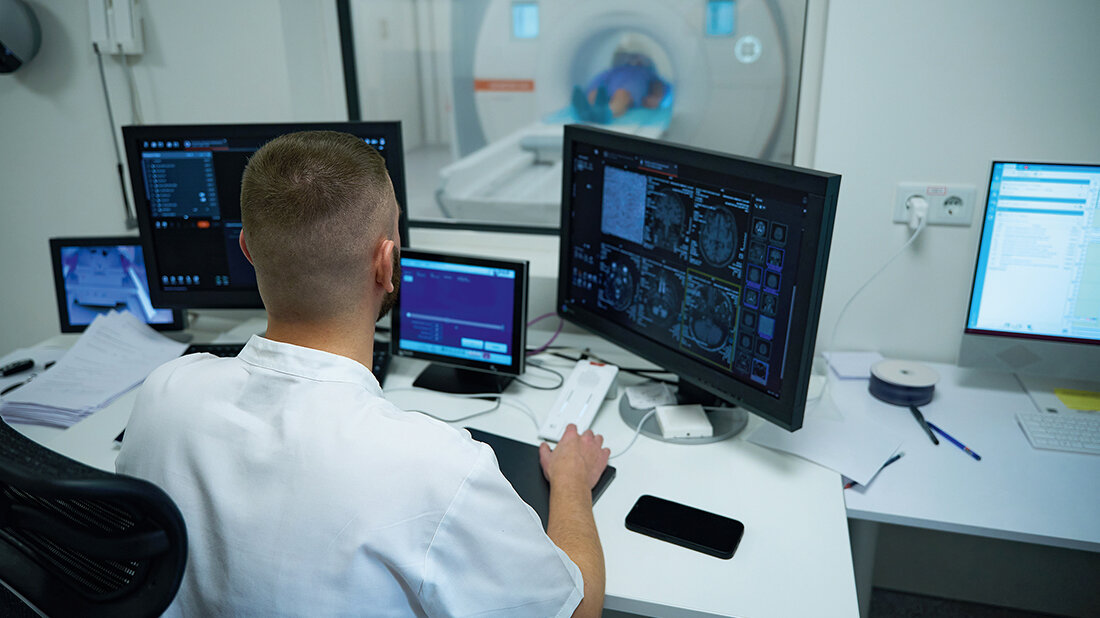 Foto eines MT an seinem Arbeitsplatz, im Hintergrund ein MRT