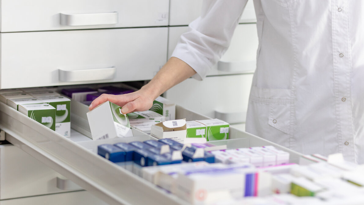 Apothekerin nimmt Medikamente aus einem Fach.
