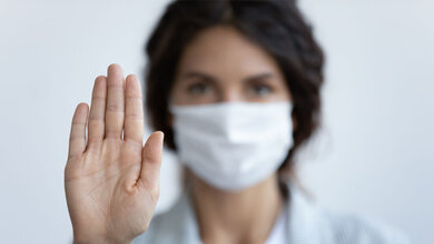 Frau miot Maske symbolisiert mit der Hand: Stopp!