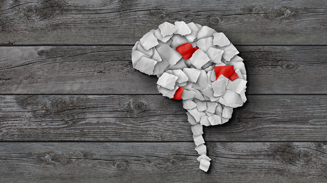 Papierschnipsel zu einem Gehirn und dem Ansatz der Wirbelsäule geformt, drei Papierschnipsel sind rot.