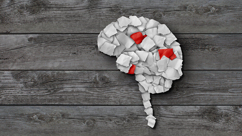 Papierschnipsel zu einem Gehirn und dem Ansatz der Wirbelsäule geformt, drei Papierschnipsel sind rot.