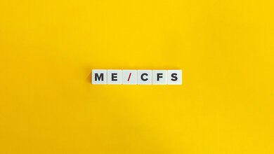 Das Foto zeigt den Begriff ME/CFS, gelegt aus Scrabble-Steinen, auf gelbem Hintergrund