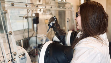 Labormitarbeiterin an einem Isolator, Hände in den Handschuhen mit Pipette und Reagenzglas in den Händen, Hintergrund verschwommen