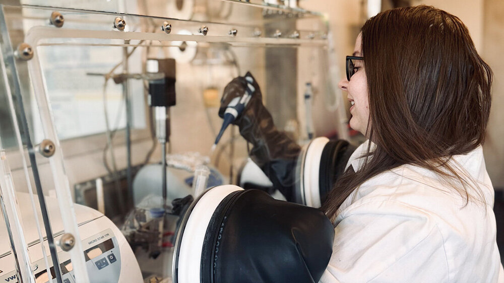 ElisabethStrunkBiophenomycine.jpg Labormitarbeiterin an einem Isolator, Hände in den Handschuhen mit Pipette und Reagenzglas in den Händen, Hintergrund verschwommen