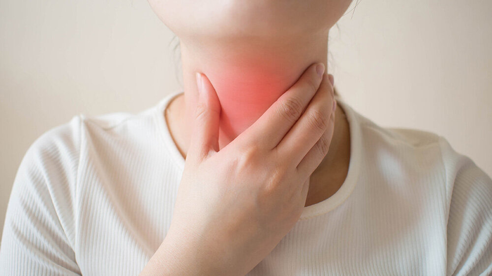 Frau hält sich den Hals mit der Hand fest, der mittig gerötet ist