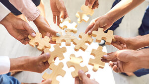 Foto, auf dem Händer Teile eines hölzernen Puzzles zusammenhalten