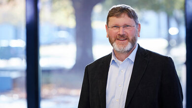 Wissenschaftler Prof. Dr. Michael Bau mit Brille und Anzug vor unscharfem Hintergrund mit Bäumen