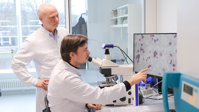 Zwei Forscher im Labor vor einem Mikroskop, dass ein Bild auf einen Bildschirm projiziert.