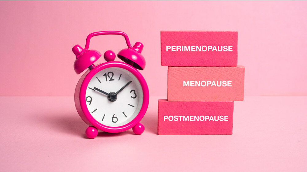 Menopause.jpg Blöcke mit den Phasen der Menopause und ein Wecker vor einem rosa Hintergrund.