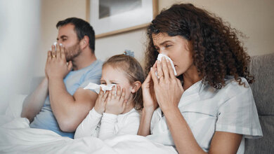 Vater, Mutter und Kind liegen krank im Bett.
