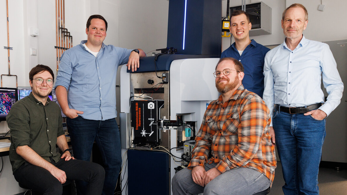 Fünf Männer, zwei links und drei rechts, vor einem modifizierten Fluoreszenzmikroskop-Massenspektrometer.