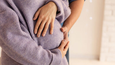 Schwangere Frau und ihr Partner umfassen den Bauch.