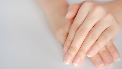 Zwei Hände, eine liegt auf der anderen auf weißem, unscharfem Hintergrund.