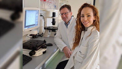 Ein Mann und eine Frau im Labor mit weißen Kitteln vor einem Mikroskop