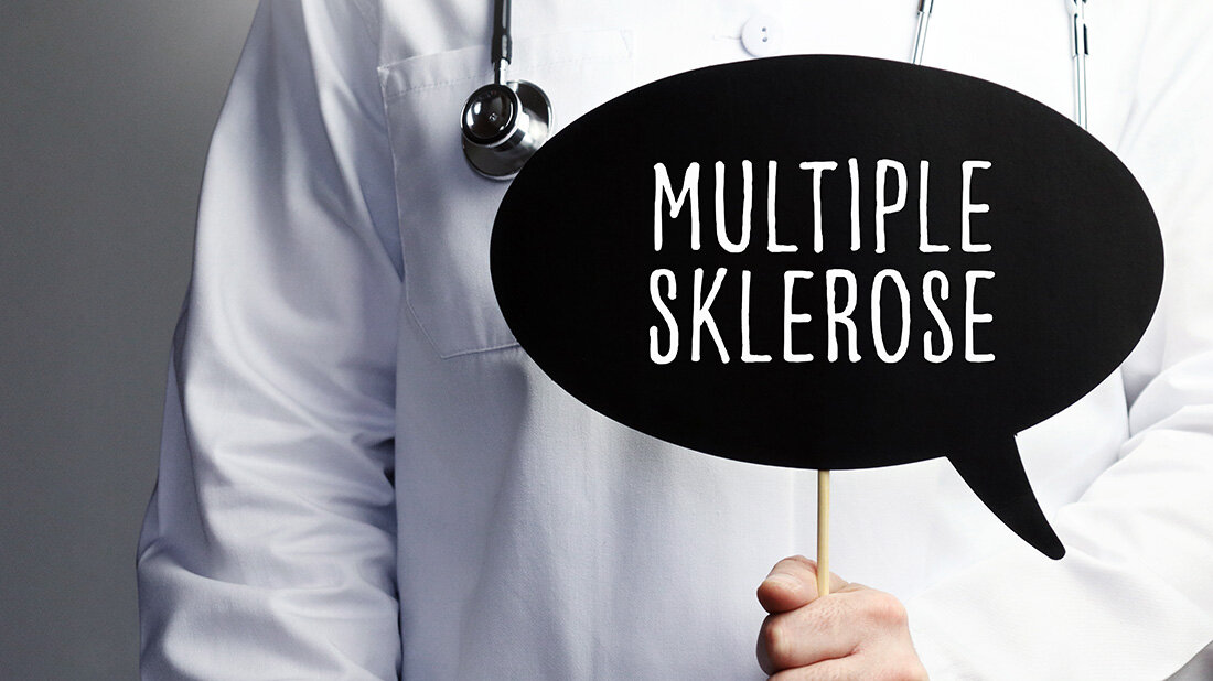 Person im Arztkittel hält ein schwarzes Schild mit der Aufschrift "Multiple Sklerose"