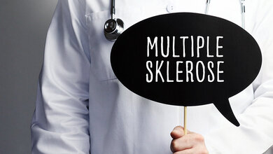 Person im Arztkittel hält ein schwarzes Schild mit der Aufschrift "Multiple Sklerose"