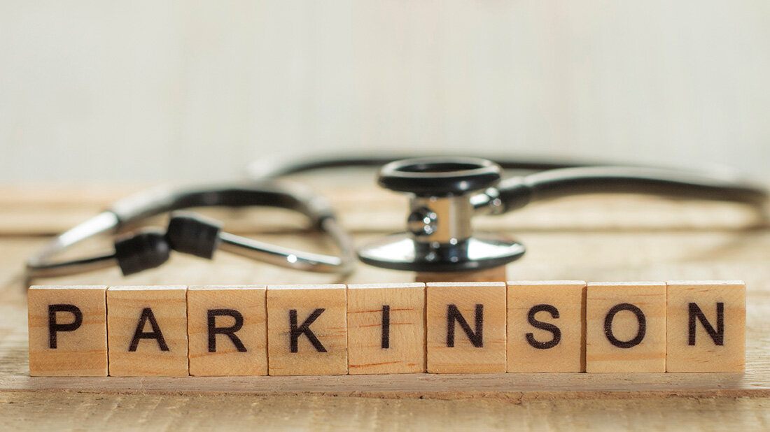 Parkinson-Schriftzug auf Holzklötzchen mit einem Stethoskop unscharf im Hintergrund.