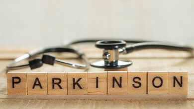 Parkinson-Schriftzug auf Holzklötzchen mit einem Stethoskop unscharf im Hintergrund.