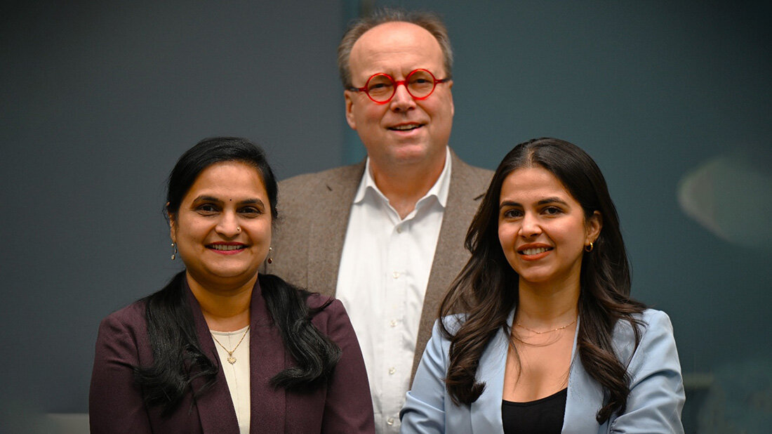 PoornimaMahavadi_AndreasGuenther_BhavikaBrahmanandKatariya.jpg Drei Personen, zwei Frauen im Vordergrund, ein Mann etwas unscharf im Hintergrund vor dunklem Hintergrund