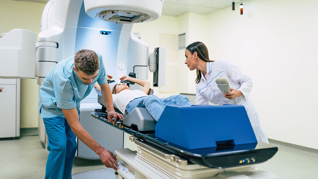 Medizinisches Fachpersonal positioniert eine Patientin auf einer modernen Strahlentherapieanlage in einem klinischen Behandlungsraum.