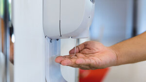 Foto eines Desinfektionsmittelspenders mit darunter gehaltener Hand