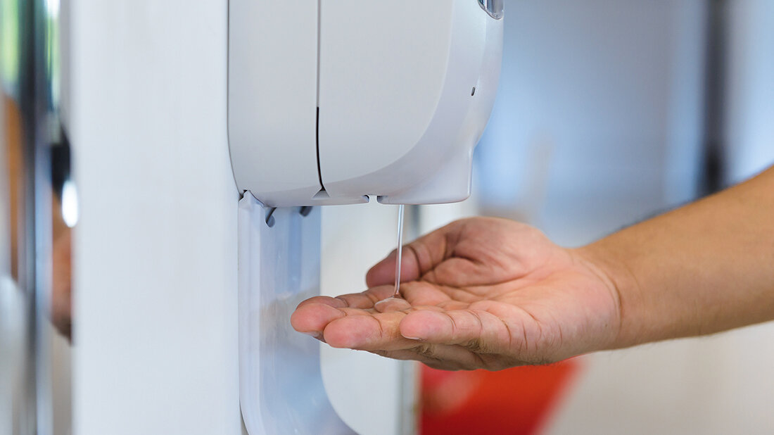 Foto eines Desinfektionsmittelspenders mit darunter gehaltener Hand