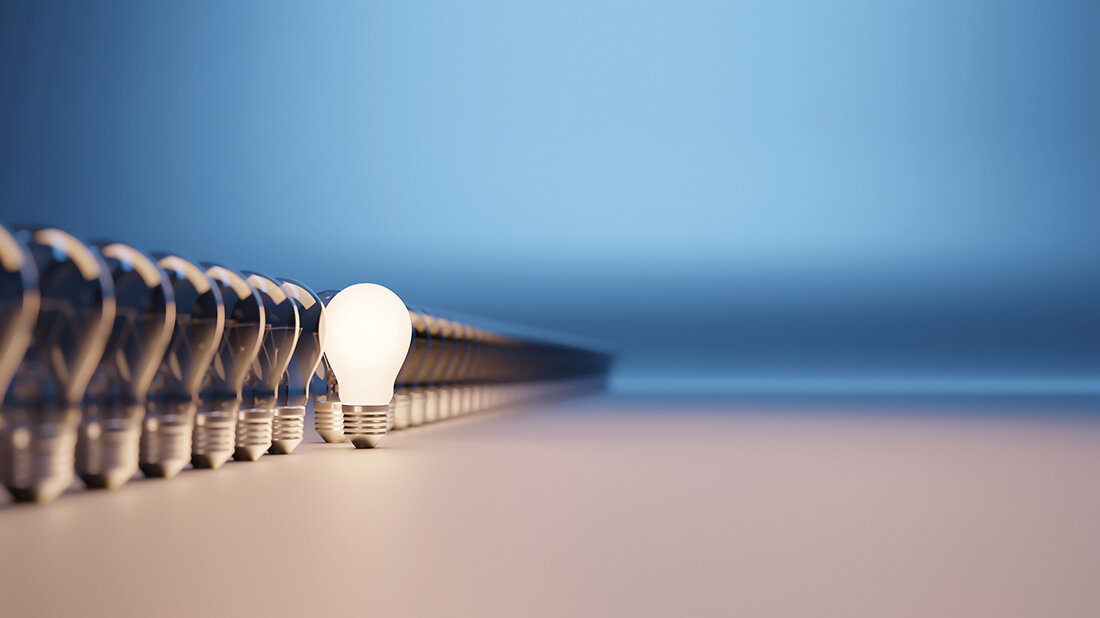 Foto einer Reihe von Glühbirnen, aus der eine einzelne leuchtende hervorsteht