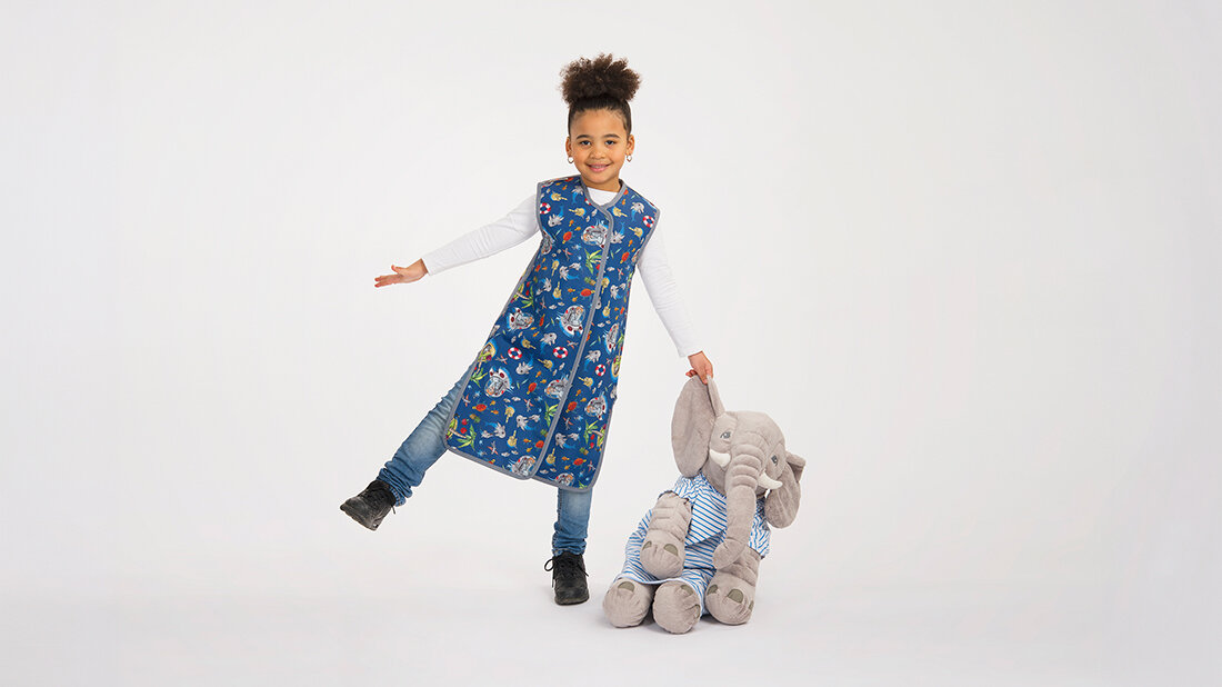 Strahlenschutzmittel in der Kinderradiologie – nicht mehr nötig? Foto eines Mädchen in einem Rundumschutzmantel, das auf einem Bein steht und einen großen Stoffelefanten festhält