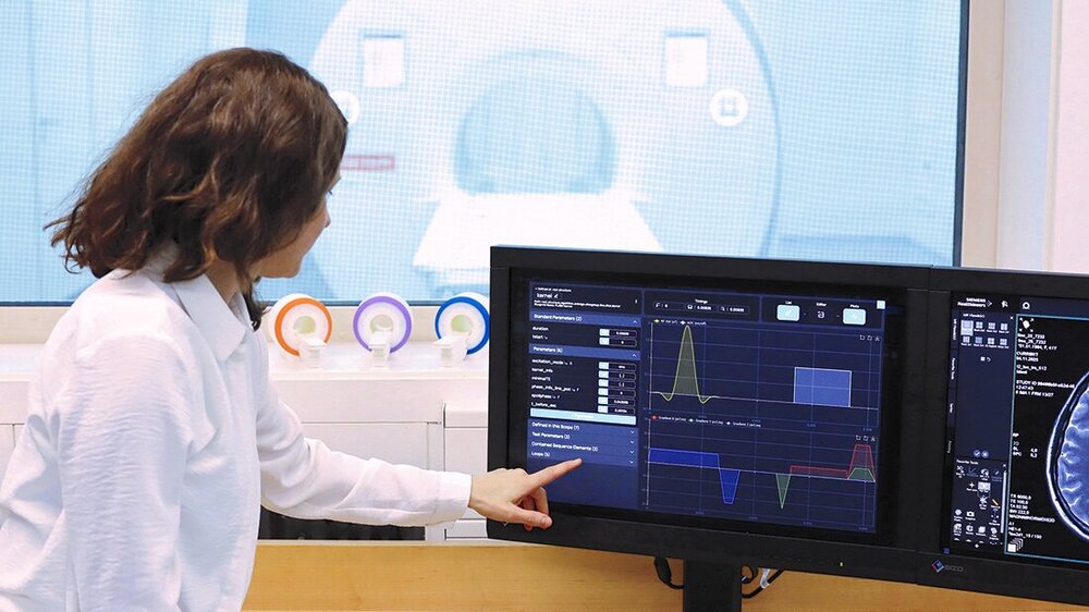 Ärztin im Vorraum des MRT, im Hintergrund zu sehen, und zeigt etwas an einem Bildschirm