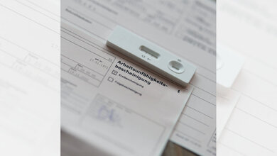 Positiver Coronatest, der auf einer Arbeitsunfähigkeitsbescheinigung liegt.