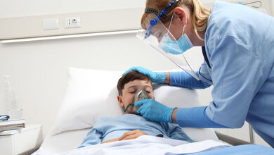 Kind mit COVID-19 bekommt in der Klinik Sauerstoff von einer Pflegerin.