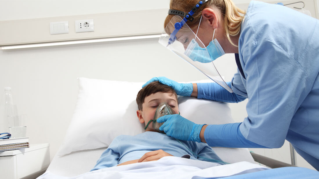 Kind mit COVID-19 bekommt in der Klinik Sauerstoff von einer Pflegerin.