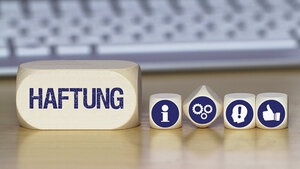 Foto mehrerer Würfel mit Symbolen und eines mit der Aufschrift „Haftung“ auf einem Schreibtisch