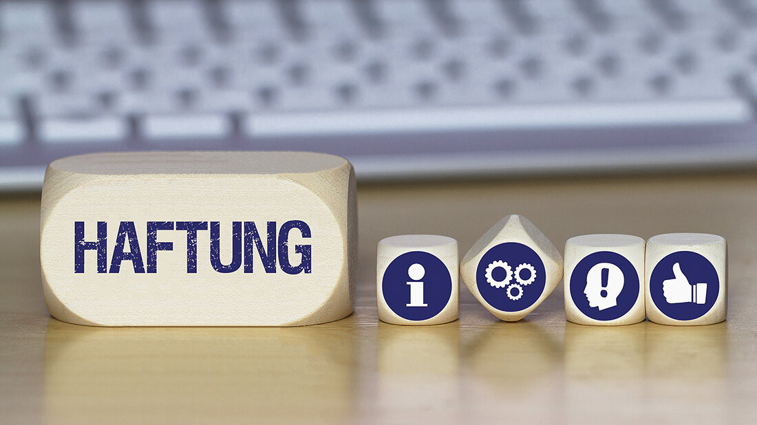 Foto mehrerer Würfel mit Symbolen und eines mit der Aufschrift „Haftung“ auf einem Schreibtisch