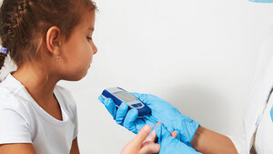 Einem Mädchen wird für einen Glykämietest Blut aus der Kuppe des rechten Mittelfingers entnommen.