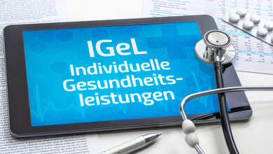 Das Bild zeigt ein Tablet, auf dessen Bildschirm der Text "IGeL - Individuelle Gesundheitsleistungen" angezeigt wird. Daneben liegen ein Stethoskop, ein Kugelschreiber und medizinische Unterlagen, die auf den Kontext des Gesundheitswesens hinweisen.