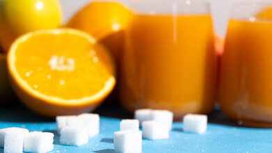 Fruchtsaft und Orangen und im Vordergund Würfelzuckerstücke.