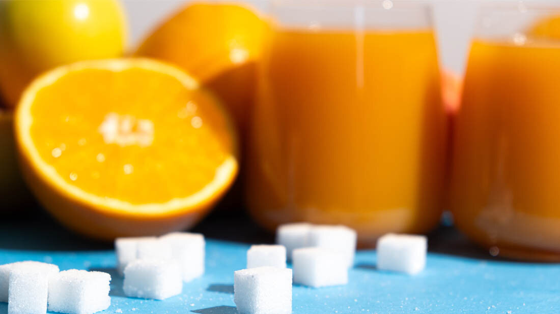 Fruchtsaft und Orangen und im Vordergund Würfelzuckerstücke.