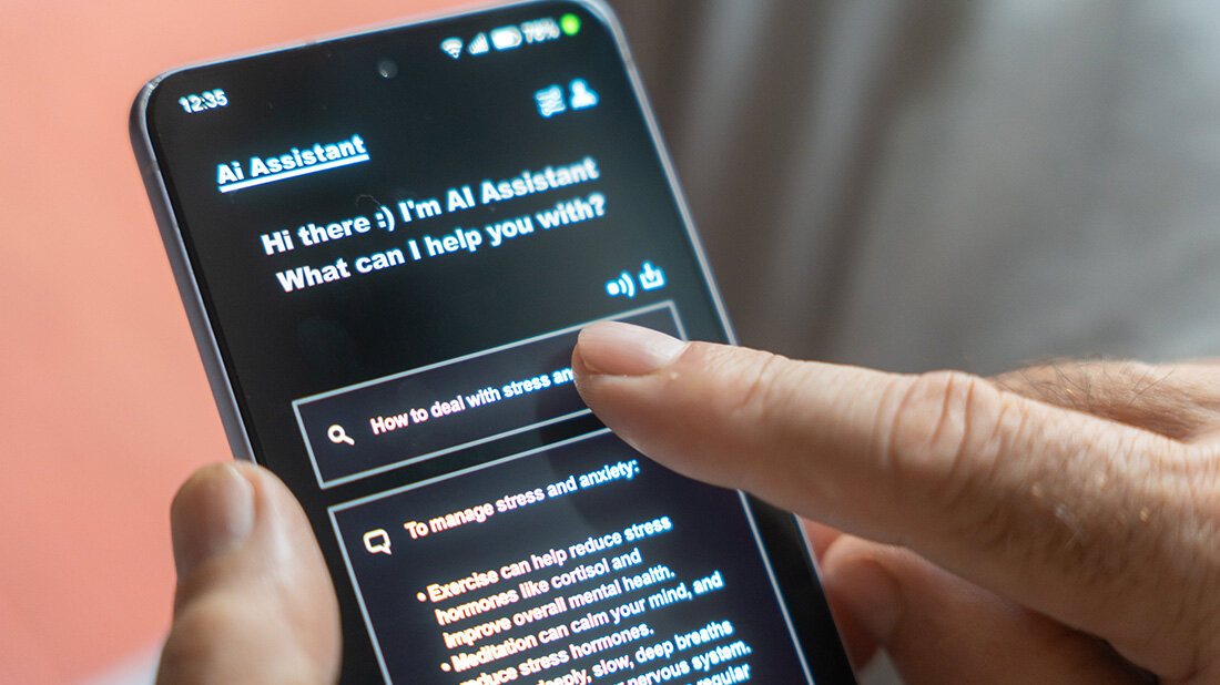 KI-Assistent_Gesundheit.jpg Smartphone mit offenem KI-Assistenten, ein Finger drückt auf den Bildschirm
