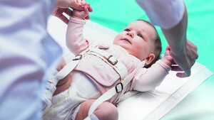 Foto eines Säuglings, dem eine Pavlik-Bandage zur Behandlung einer Hüftgelenksdysplasie angelegt wird
