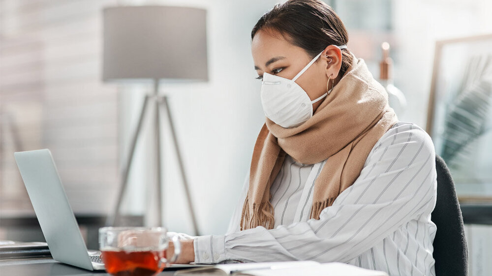 Kranke Frau mit Maske sitzt am PC.