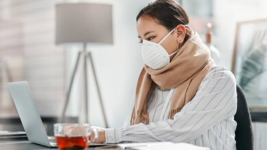 Kranke Frau mit Maske sitzt am PC.